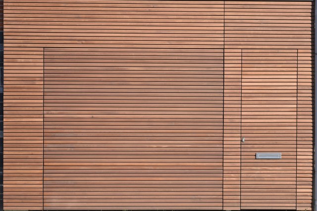 WOOD Collection : habillage de façade en bois massif Venti avec porte sectionnelle et porte d'entrée